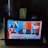 A tablet screen displays a CNN news segment showing results for the 2020 U.S. presidential election with Joe Biden elected president. The broadcast features six separate images of people, including a central anchor and participants in smaller screens. The headline reads 'BREAKING NEWS' and discusses Trump's lack of public acceptance. The setup includes a lit white lamp on the left and a box of crackers sitting behind the tablet.